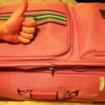 a hand giving a thumbs up on a pink suitcase